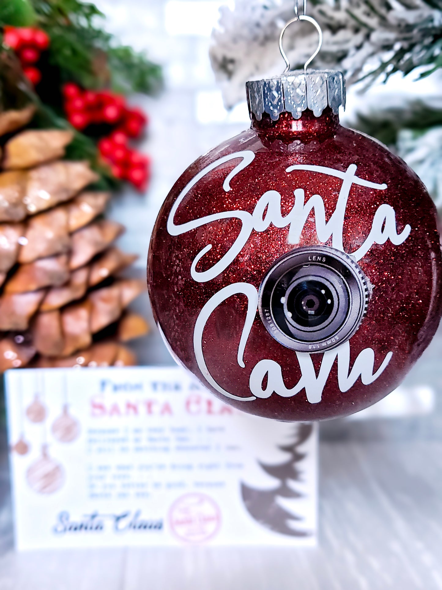 Handcrafted Santa Cam Ornament with a sparkling red finish, faux camera lens, and a letter from Santa Claus, perfect for adding magic to holiday décor.