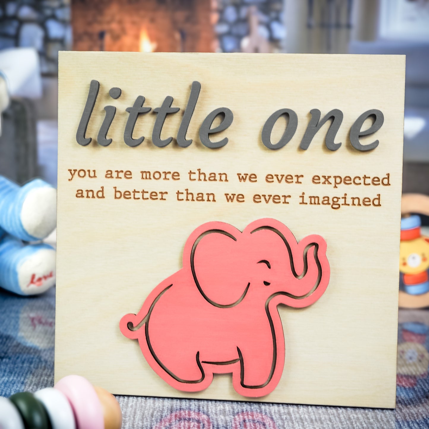 Light wood sign featuring the phrase "little one you are more than we ever expected and better than we ever imagined" with raised gray text and a pink elephant cutout at the bottom.
