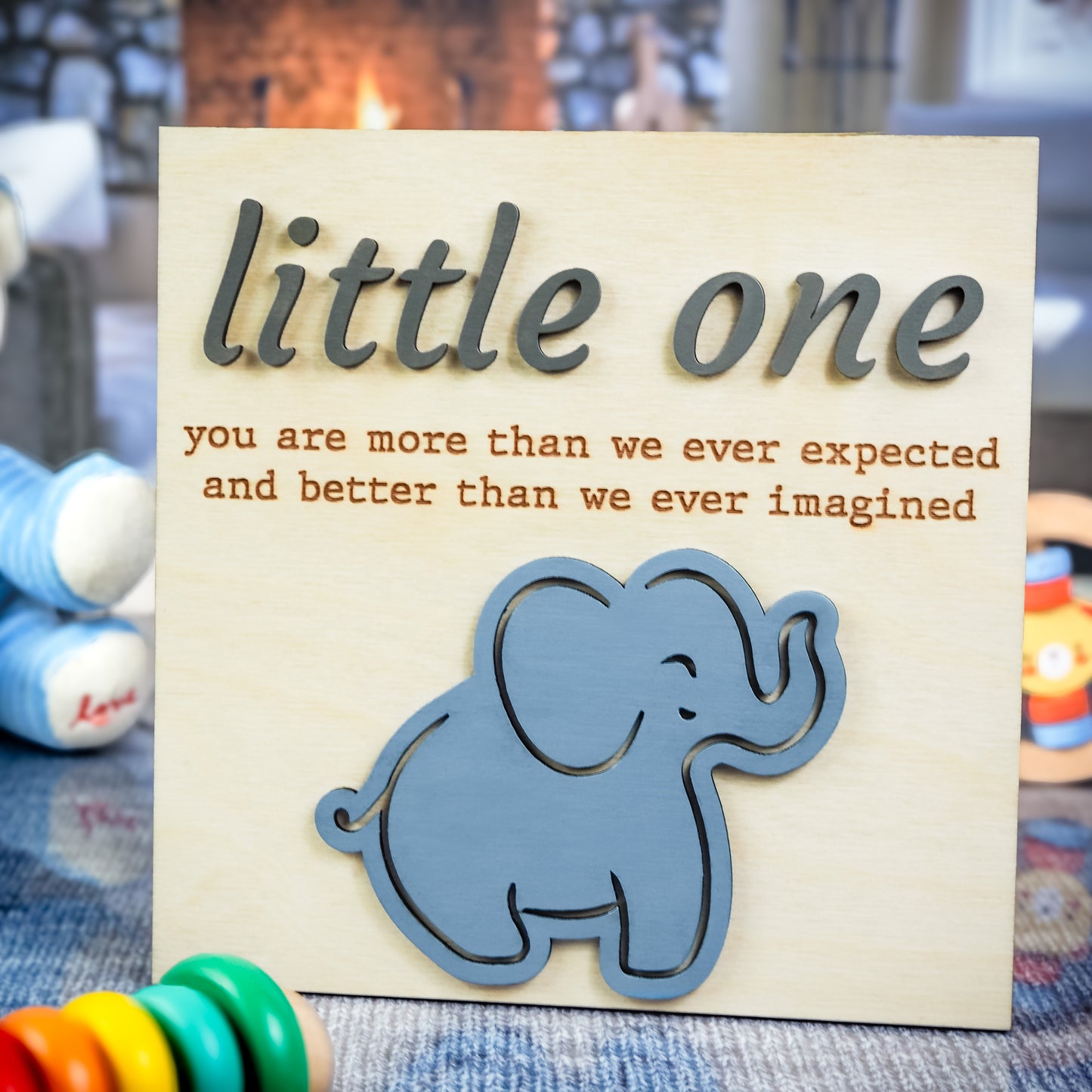 Light wood sign featuring the phrase "little one you are more than we ever expected and better than we ever imagined" with raised gray text and a blue elephant cutout at the bottom.