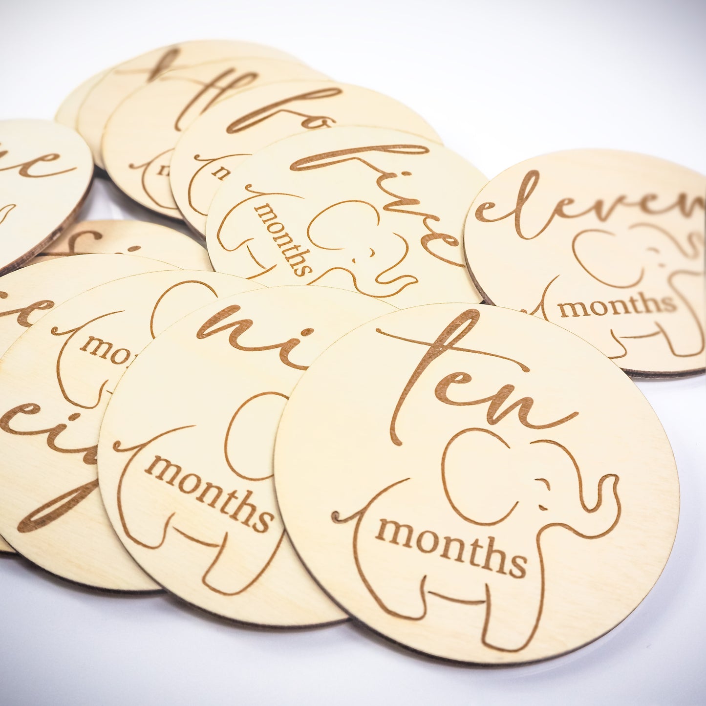 Set of engraved wooden baby milestone discs featuring an elephant design and labeled with months five through eleven.