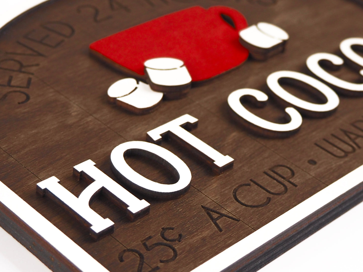 Close-up of a rustic "Hot Cocoa" sign with bold white lettering and raised details. The red mug and marshmallows add a charming touch, with the text "25¢ a cup" and “Warm up here” clearly visible against the woodgrain background.