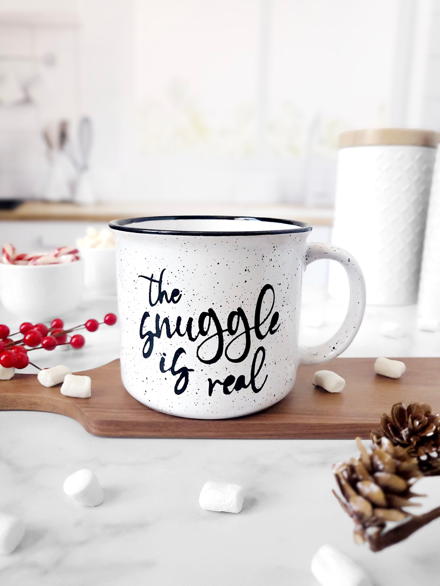 White speckled ceramic campfire mug with a black rim. The mug features the text the snuggle is real in black, playful script font.