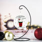 White round ornament with the text "It's Beginning to Look a Latte Like Christmas" and a raised red coffee cup design featuring whipped cream, a candy cane, and snowflakes. The background includes festive holiday décor and ornaments in black, gold, and red.