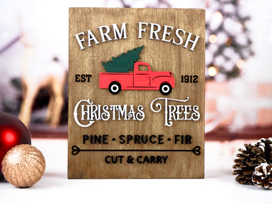 Farm Fresh Christmas Trees sign featuring a red vintage truck carrying a green Christmas tree, with raised text reading "Est 1912" and "Pine, Spruce, Fir." The background is rustic wood, and "Cut & Carry" is displayed in black at the bottom.