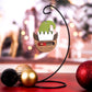 Wooden Christmas ornament shaped like an elf hat with a slider, showing options for "Naughty" or "Nice." The ornament is hung on a black display hook, surrounded by red, gold, and black baubles, set against a festive background.