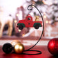 Ornament in the shape of a red vintage truck with a dog sitting in the back, hanging on a display stand with a festive holiday background.