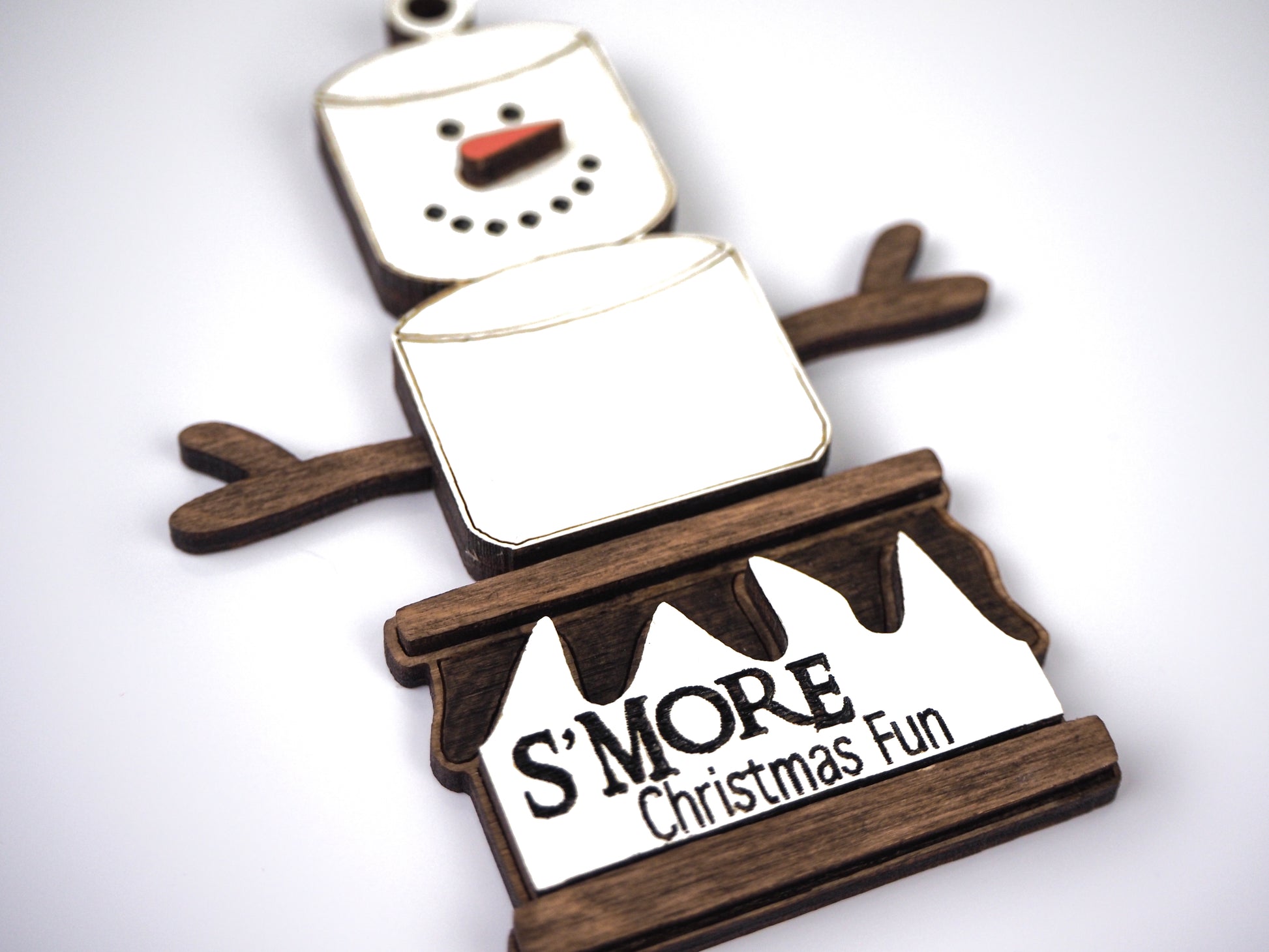 Close-up of a snowman ornament made of marshmallows, with twig-like arms and a wooden base that reads "S'MORE Christmas Fun."