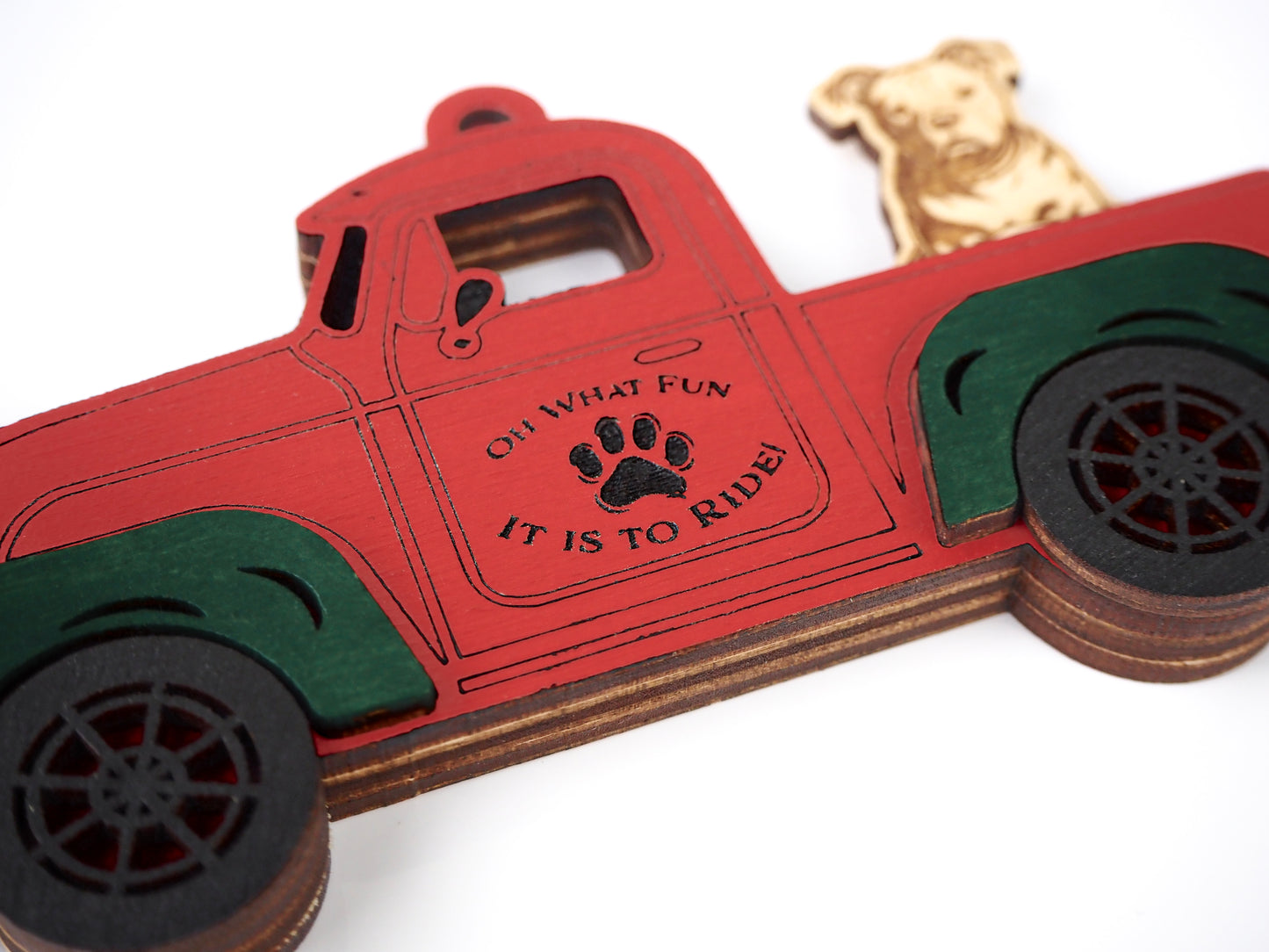 Close-up of a red truck ornament with green fenders, featuring a dog sitting in the truck bed. The door reads "Oh What Fun It Is To Ride" with a paw print design.