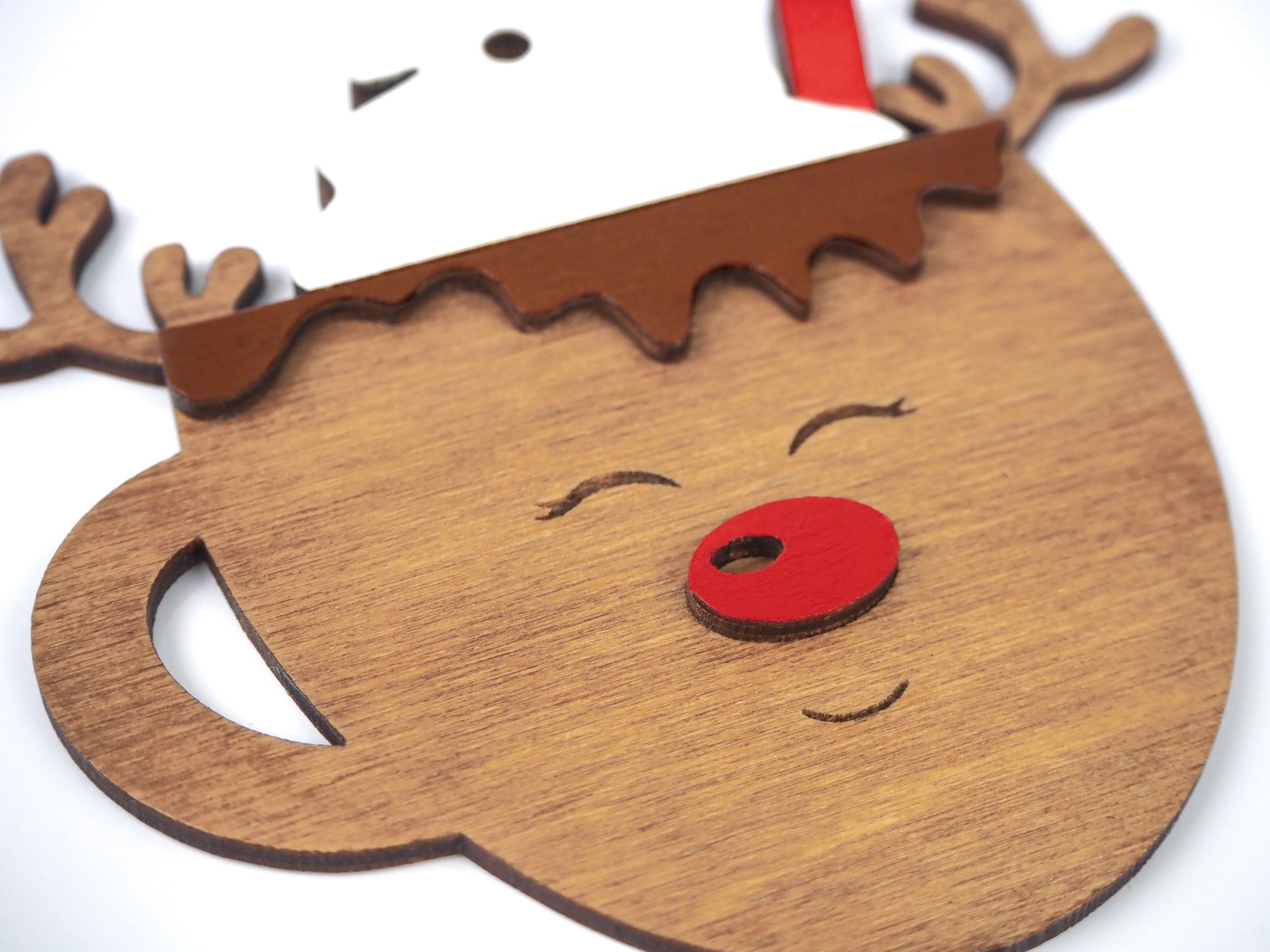 Close-up of a reindeer-themed mug ornament, featuring carved wooden antlers, a red nose, and a white whipped cream design at the top.