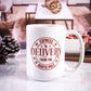 White ceramic mug with "Express Delivery from the North Pole" printed in red, featuring festive snowflakes and a reindeer. The background shows a cozy living room setup with pinecones and candy canes.