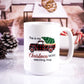 White ceramic mug with "This is my Christmas Movie Watching Mug" text featuring a red buffalo plaid truck carrying a Christmas tree. Cozy living room setting in the background with pinecones and candy canes.