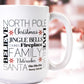 White ceramic mug featuring a collage of festive words like "North Pole," "Jingle Bells," "Santa," "Family," and "Nutcracker" in black and red text. The background includes a cozy holiday scene with blurred Christmas décor.