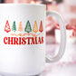 White ceramic mug with a colorful "Merry Christmas" design featuring red, green, yellow, and orange stylized Christmas trees above the text, set against a blurred festive background.