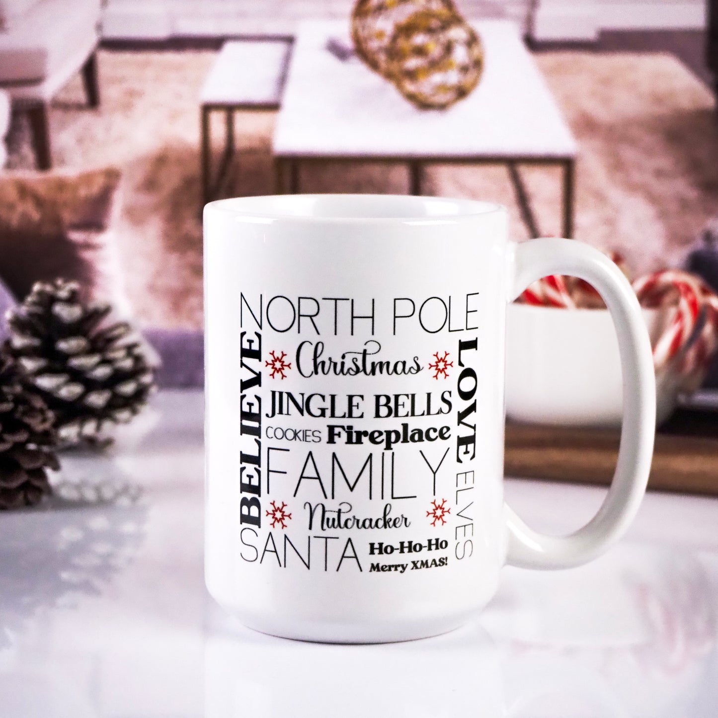 White ceramic mug featuring a festive word collage with phrases like "North Pole," "Jingle Bells," "Cookies," "Nutcracker," "Fireplace," and "Santa," displayed in various fonts and sizes. The mug is set against a cozy, blurred festive background.