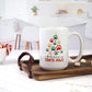 White ceramic mug featuring a colorful Christmas tree design made of paw prints in red, green, and orange, with the words "I Believe in Santa Paws" below. The mug is placed on a wooden tray in a bright kitchen setting, with marshmallows and candy canes nearby.