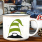 White speckled ceramic campfire mug with a black rim. The mug features a whimsical gnome design, with the gnome wearing a green and white striped hat that covers its eyes, with only the black nose and part of the beard visible.