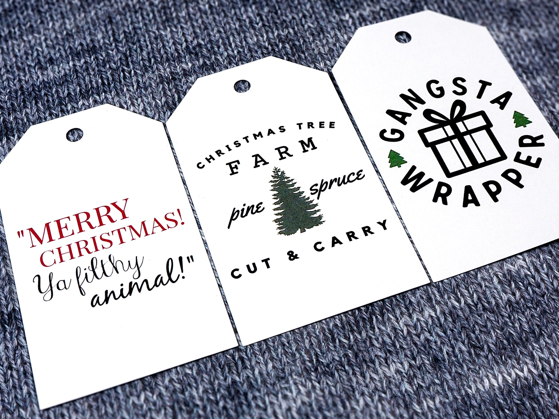 Three white rectangular Christmas gift tags. The first tag reads Merry Christmas Ya Filthy Animal! in red and black text. The second tag features a Christmas Tree Farm Pine Spruce Cut & Carry design with a tree. The third tag displays the phrase Gangsta Wrapper with a gift box and 2 small tree accents.