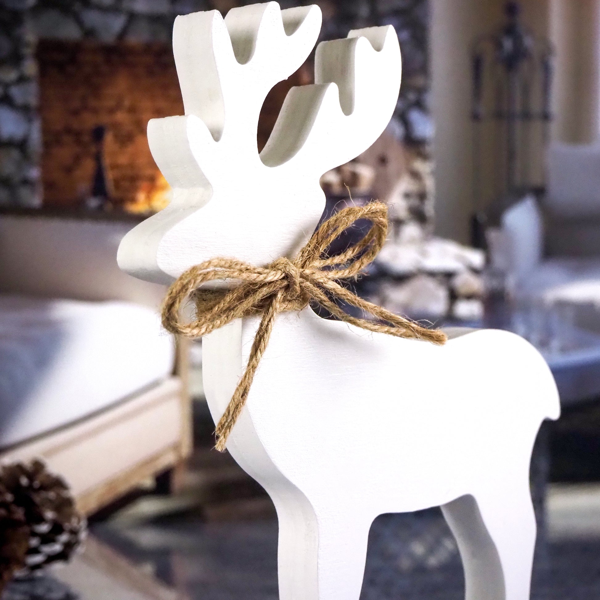 White wooden reindeer with a twine bow around its neck, set in a cozy living room scene with a stone fireplace in the background.