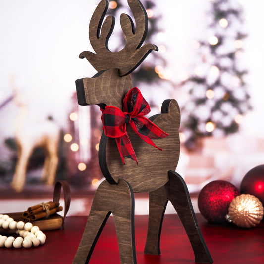 Rustic wooden reindeer with a red and black plaid bow, displayed against a festive holiday backdrop featuring Christmas trees, ornaments, and cinnamon sticks.