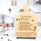 Wooden cutting board-style decoration engraved with a whimsical Christmas recipe, featuring festive text and illustrations like a sleigh, snowflake, and candy cane, displayed on a stand in a bright, modern kitchen setting.