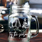 Clear glass mason jar-style mug with a handle. The mug features three white, stylized Christmas trees in a row at the top. Below the trees, the text 'Tis the season is written in a white, flowing script.