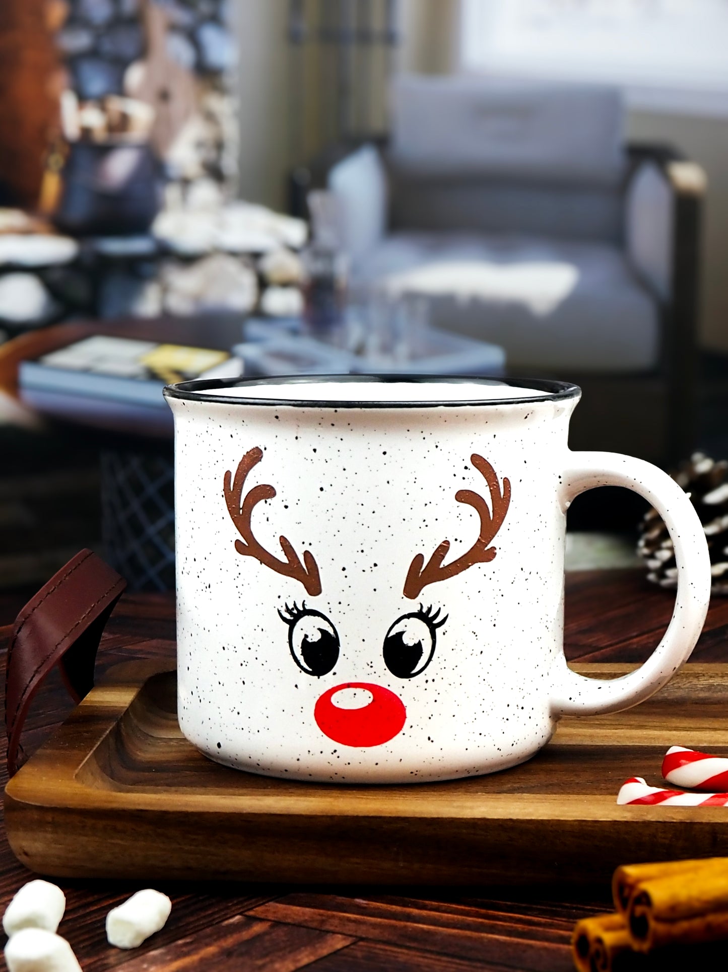 White speckled ceramic campfire mug with a black rim, featuring a reindeer face design. The face includes large black eyes, brown antlers, and a bright red nose, resembling Rudolph the Red-Nosed Reindeer.