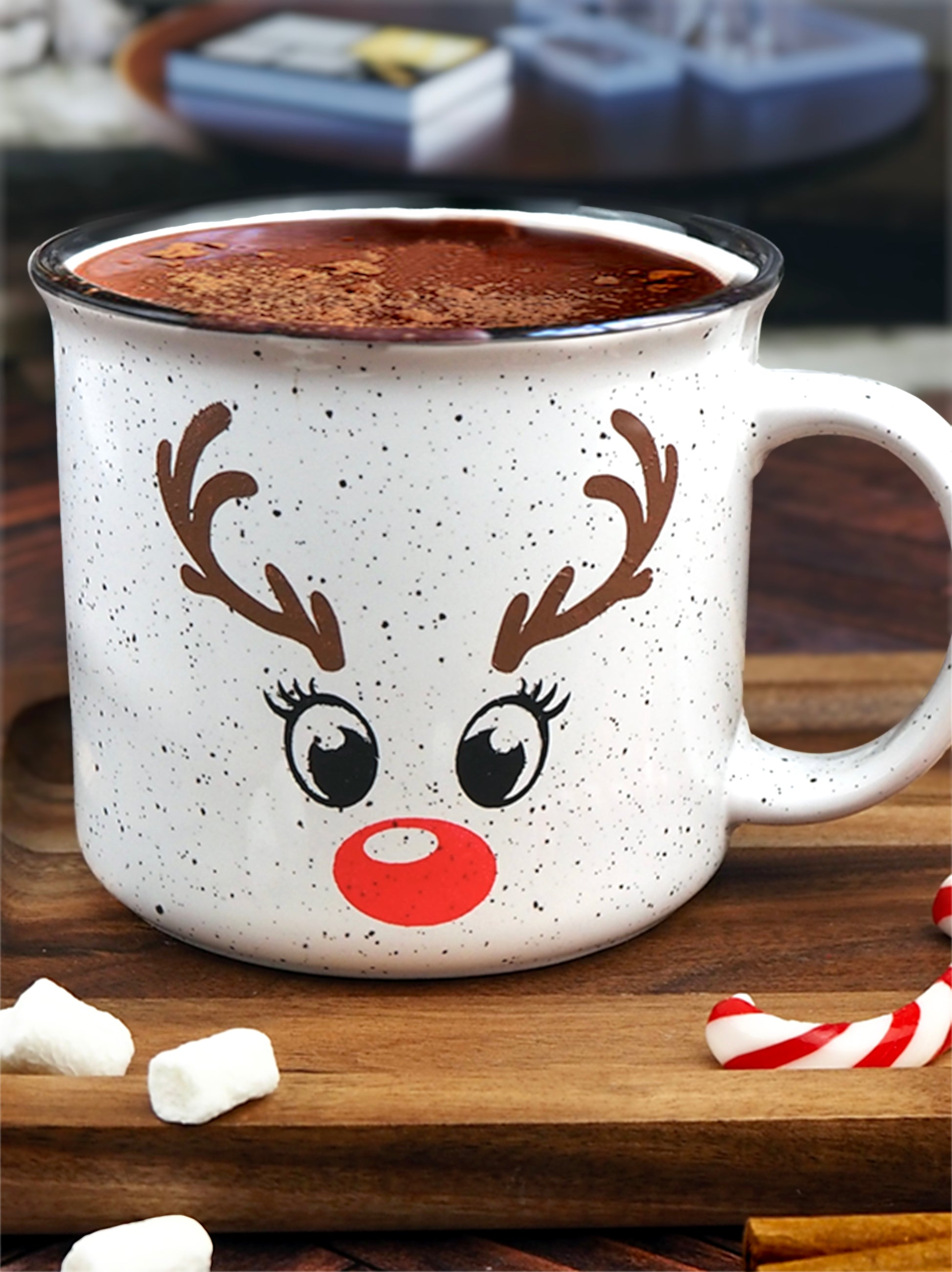 White speckled ceramic campfire mug with a black rim, featuring a reindeer face design. The face includes large black eyes, brown antlers, and a bright red nose, resembling Rudolph the Red-Nosed Reindeer.