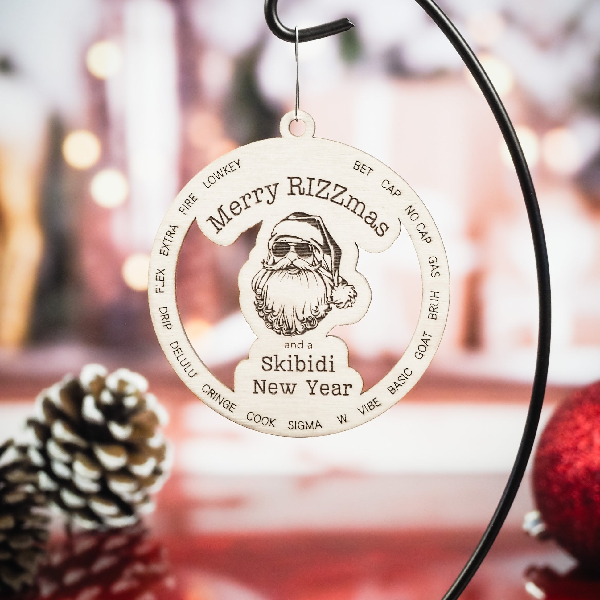 Wooden Christmas ornament featuring the phrase Merry Rizzmas and a Skibidi New Year, with a detailed Santa wearing sunglasses. Surrounding the Santa are trendy slang words engraved in a circular design. The ornament is displayed on a black metal stand with a blurred festive background, including pinecones and holiday decor.