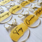 3-inch acrylic discs with gold hand-painted on the back, a personalized name written on the front in black and a gold ribbon tied in a bow. Handmade by Snuggle Up Co.