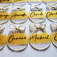 3-inch acrylic discs with gold hand-painted on the back, a personalized name written on the front in black and a gold ribbon tied in a bow. Handmade by Snuggle Up Co.