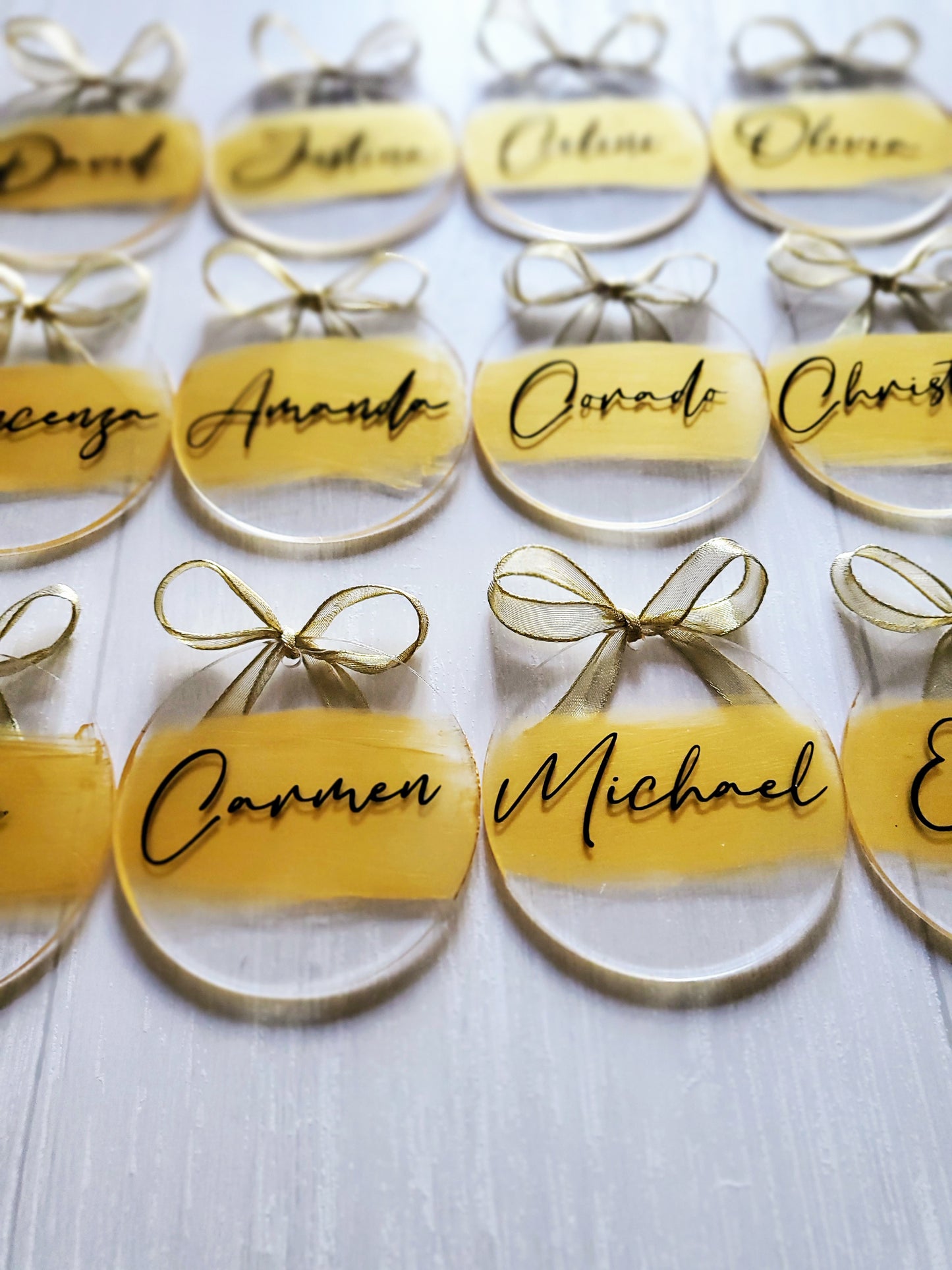 3-inch acrylic discs with gold hand-painted on the back, a personalized name written on the front in black and a gold ribbon tied in a bow. Handmade by Snuggle Up Co.