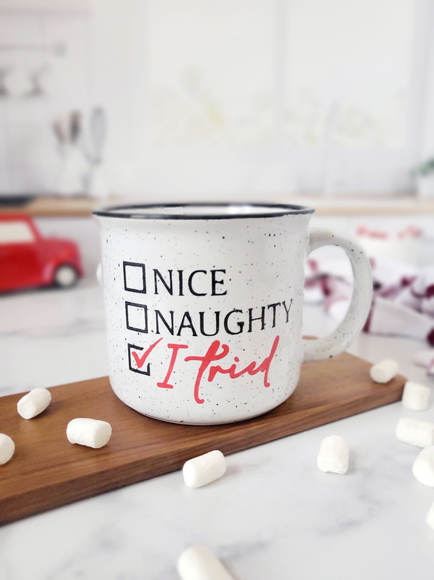 Campfire white ceramic mug with speckles and a black halo around the rim. The words Nice, Naughty and I tired are hand-painted with a check mark beside I tried is on one side. Nice and Naughty is painted in black and the checkmark and I tried is painted in red. The Nice, Naughty and I tried is hand-painted by Snuggle Up Co.