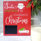 Red wooden sign with white and green lettering that reads Santa stop here! Countdown to Christmas. The sign features a chalkboard area for writing numbers and includes a white truck graphic carrying a green Christmas tree. There is also an illustration of Santa's face with a candy cane in the design.