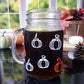 The back of the glass mason jar-style mug is decorated with 6 white and orange pumpkin graphics arranged in rows around the mug.
