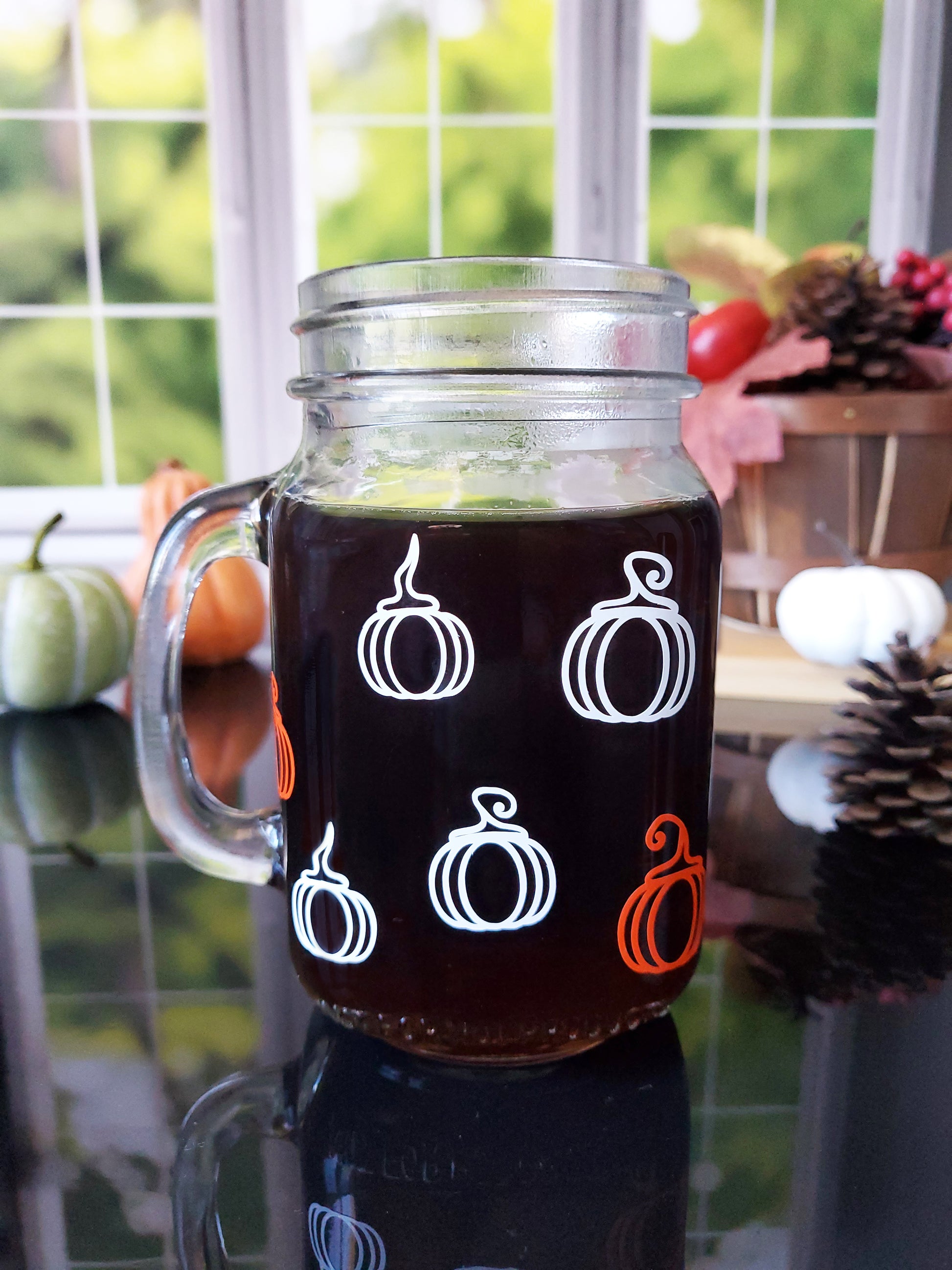 The back of the glass mason jar-style mug is decorated with 6 white and orange pumpkin graphics arranged in rows around the mug.