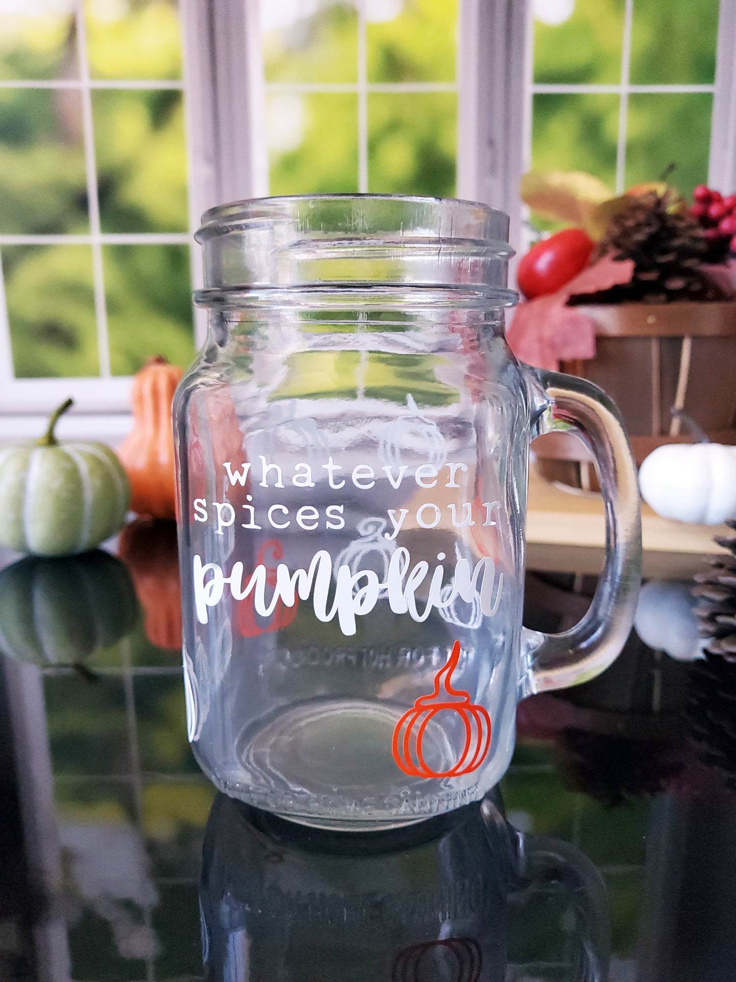 Clear glass mason jar-style mug with a handle. The mug features white text that reads "Whatever spices your pumpkin," along with an orange pumpkin graphic at the bottom.